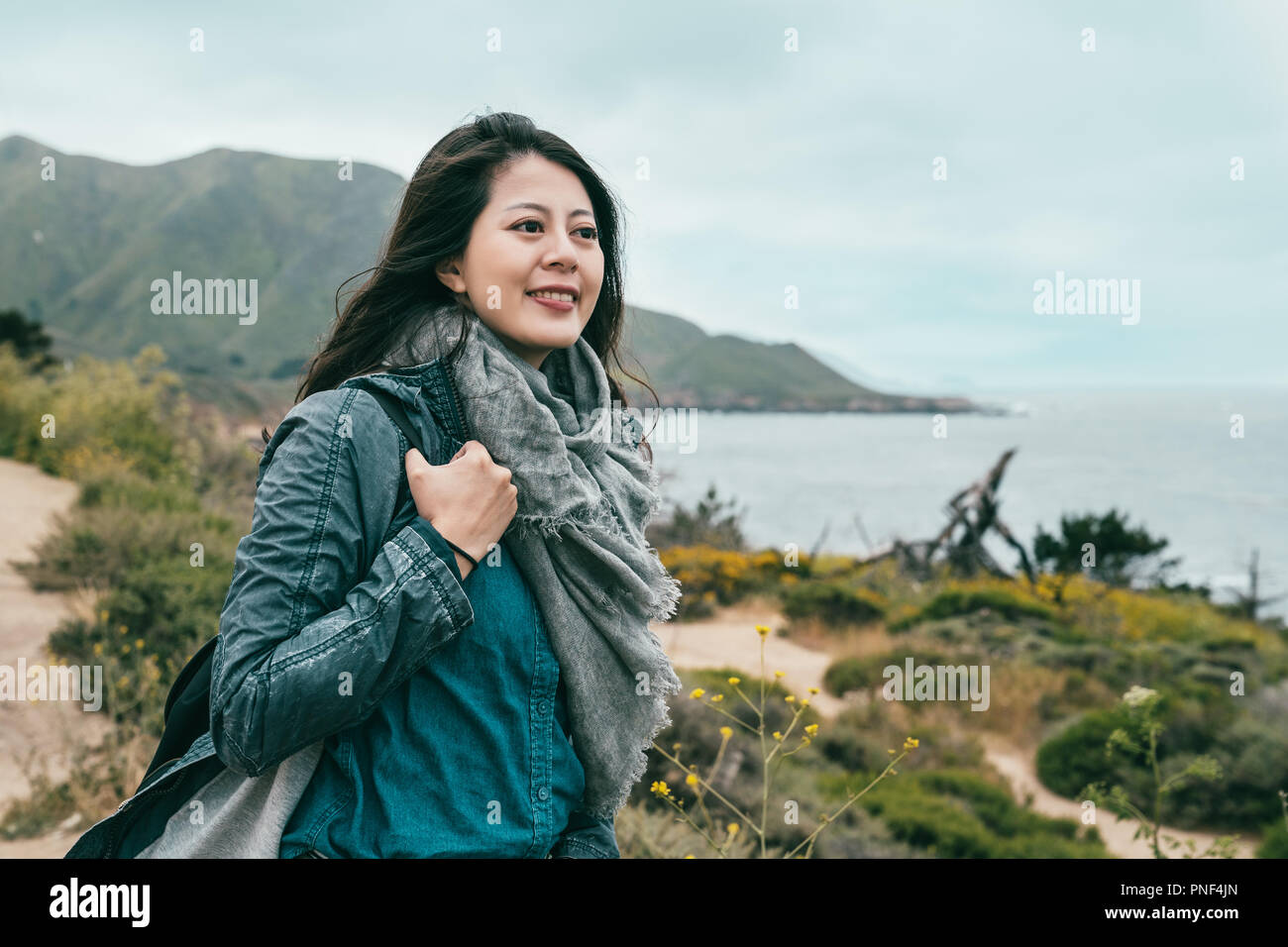 beautiful woman looking happy and standing on the coast near to the brilliant ocean and mountains. Stock Photo