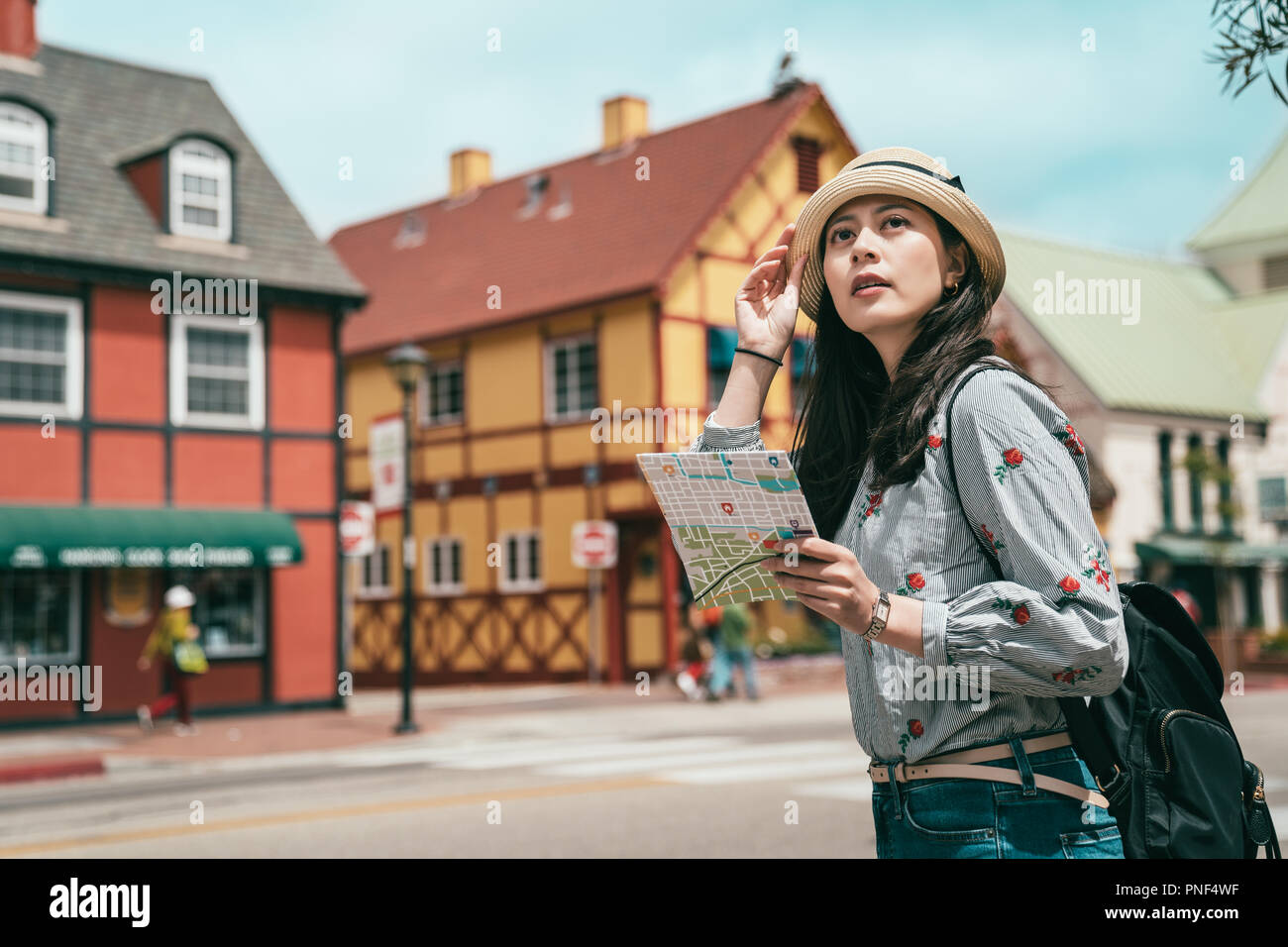 a pretty asina woman having sightseeing with a map while stepping in a lovely and beautiful old town. Stock Photo