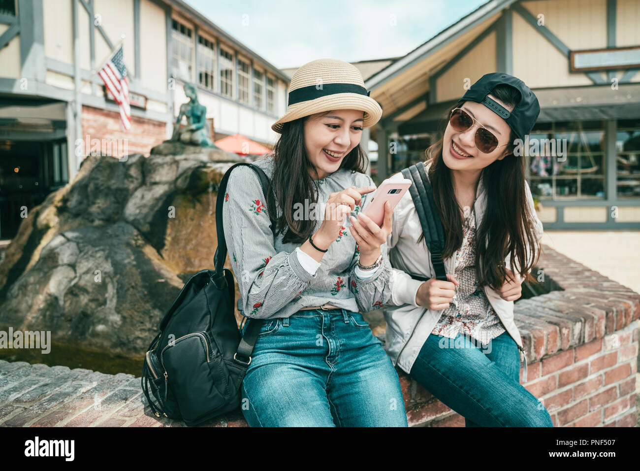 two happy girls talking and laughing joyfully while taking a break sitting next to the fountain Stock Photo
