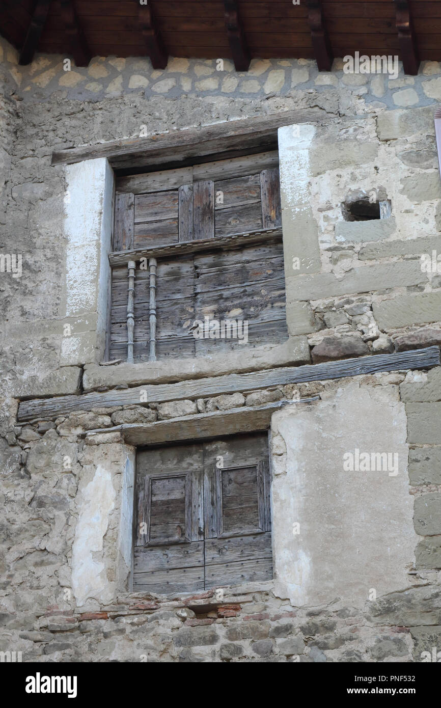 Two small windows with old shabby wooden shutters and a railing on a stone grey houses in Biel, a small town in Aragon, Spain Stock Photo