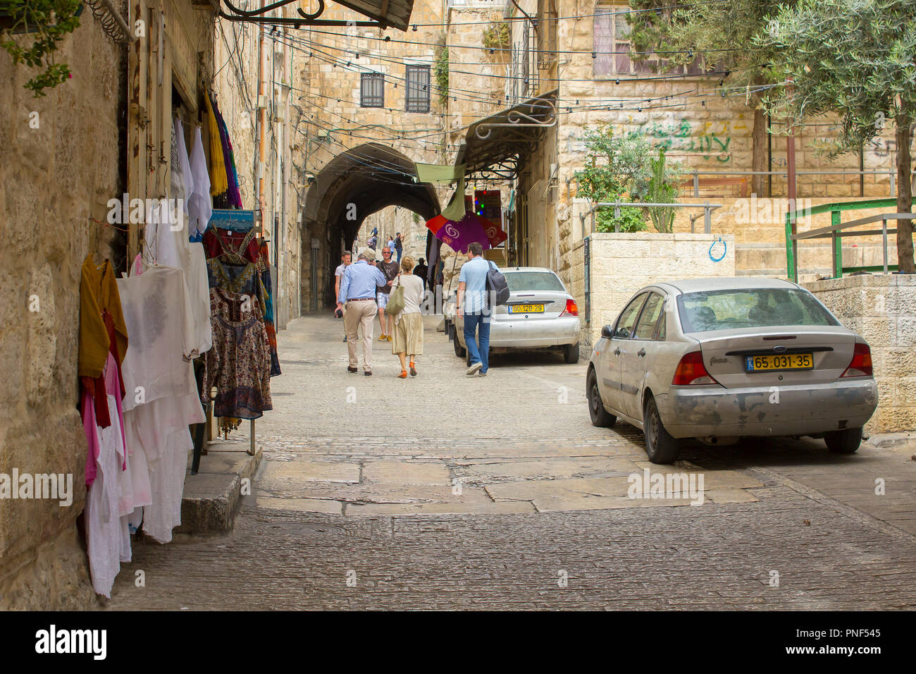 10 May 2018 Tourists strolling up the narrow Lions Gate Street in the old city Jerusalem Israel. The street has parked cars and shop goods on display  Stock Photo