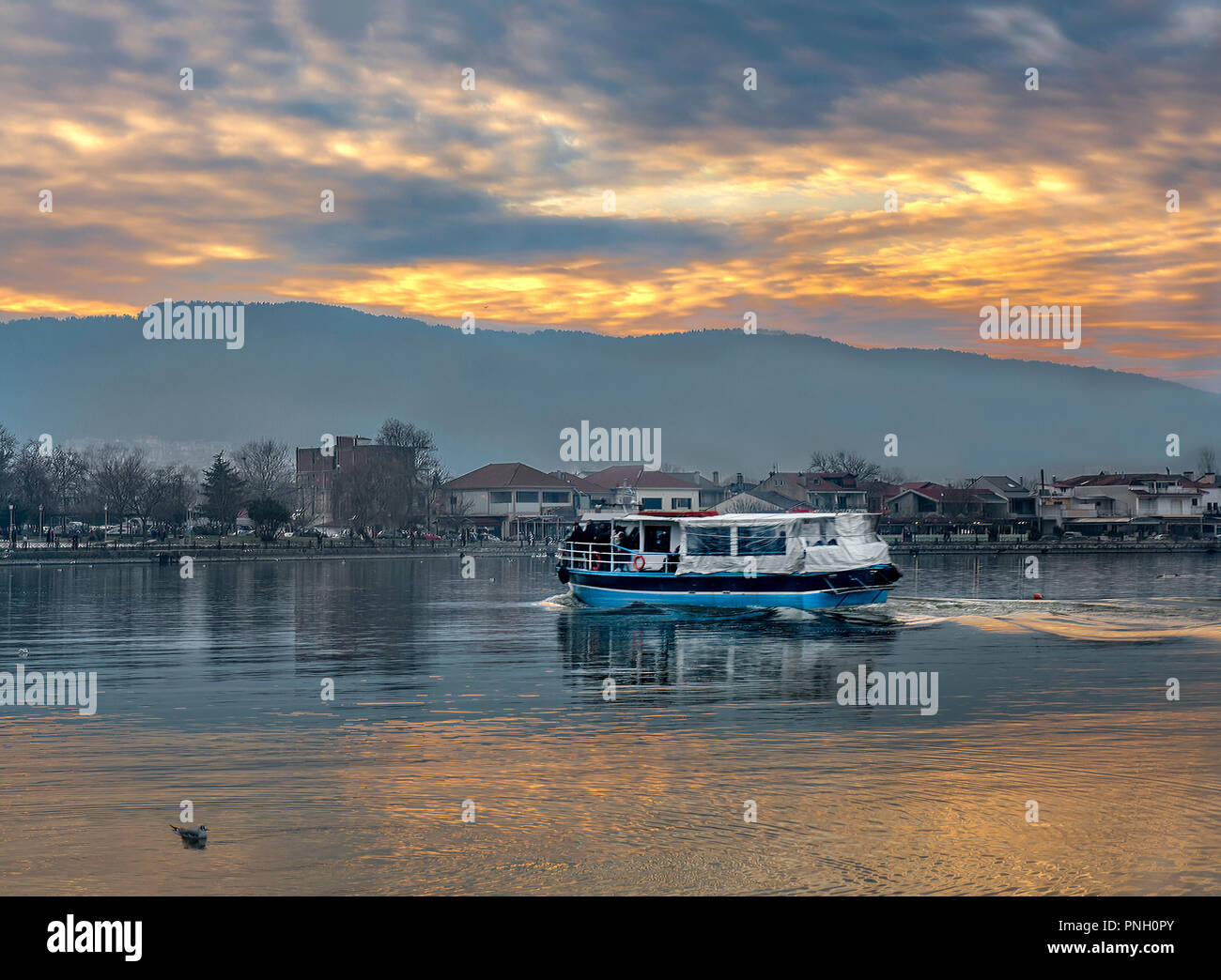 Sunset on Ioannina city. Small wooden boat floating the calm waters on lake Pamvotis and transfer passengers to a  very small island inside the lake.  Stock Photo