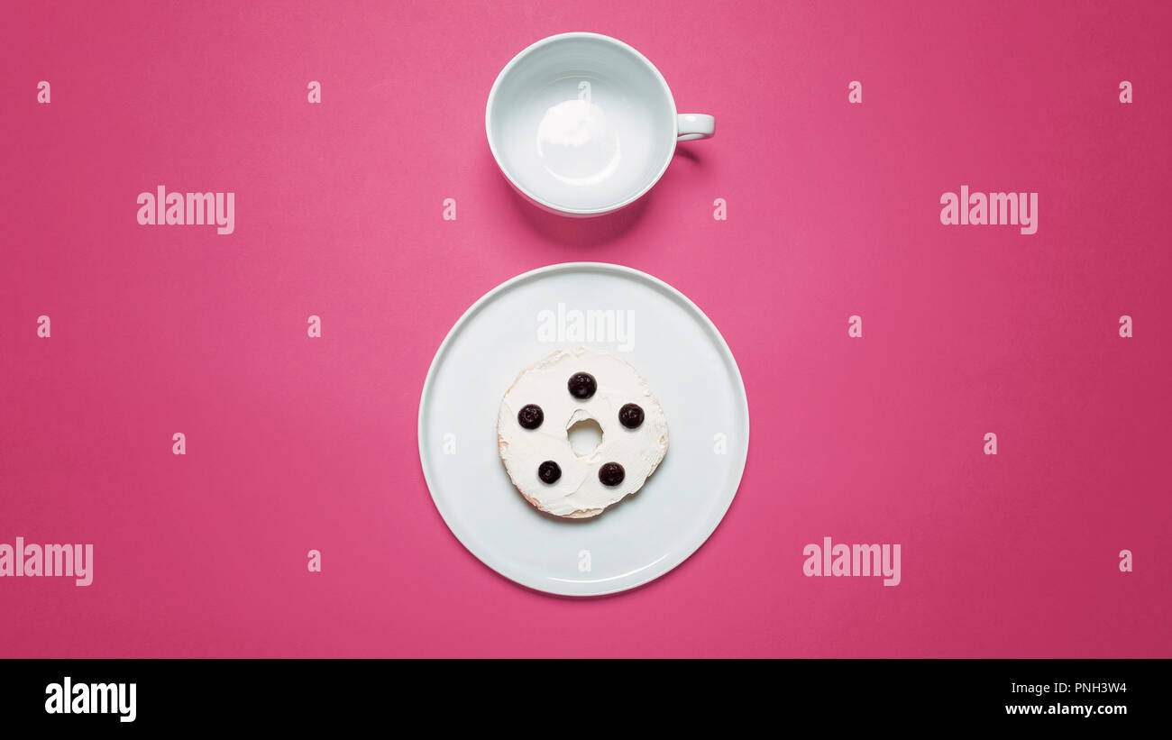 Half bagel with cream cheese and blueberries on a white plate with an empty coffee cup on a pink background Stock Photo