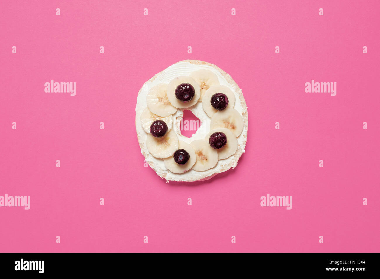 Half bagel with cream cheese, blueberries, and sliced bananas on a pink