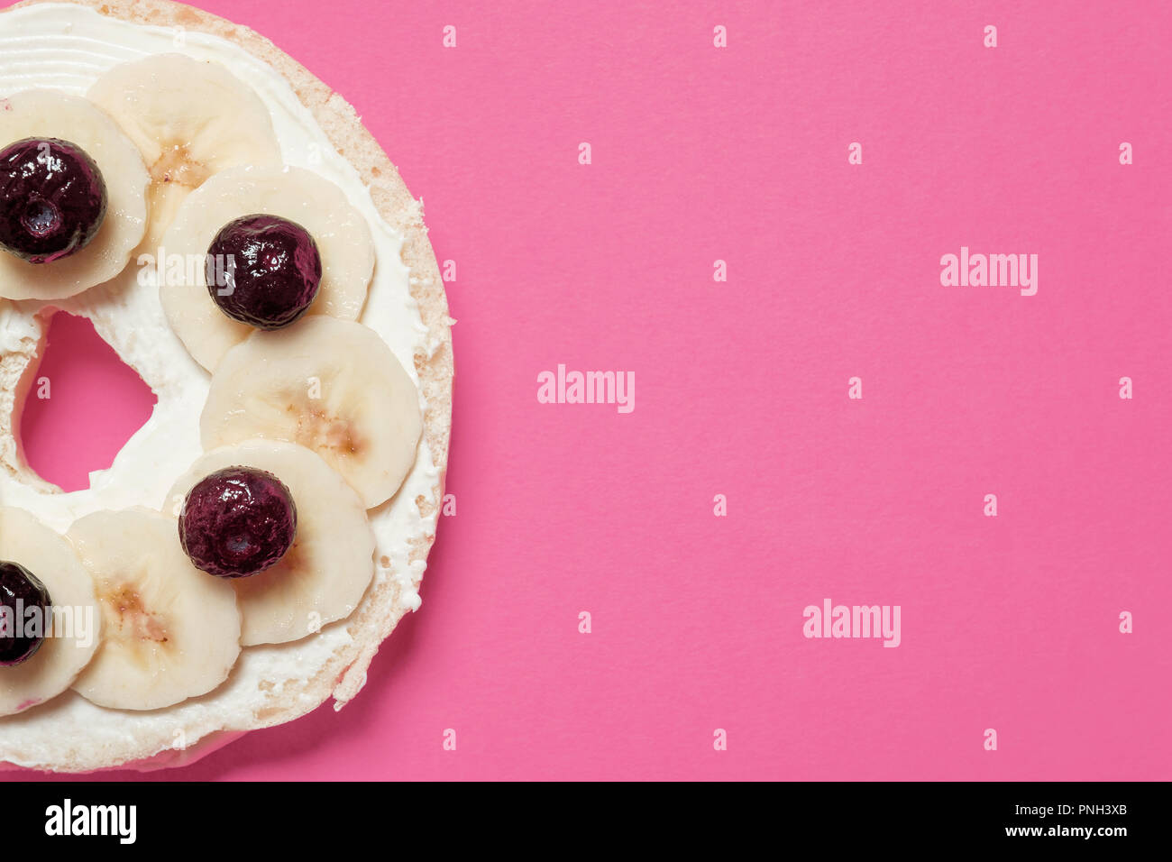 Half bagel with cream cheese, blueberries, and sliced bananas on a pink