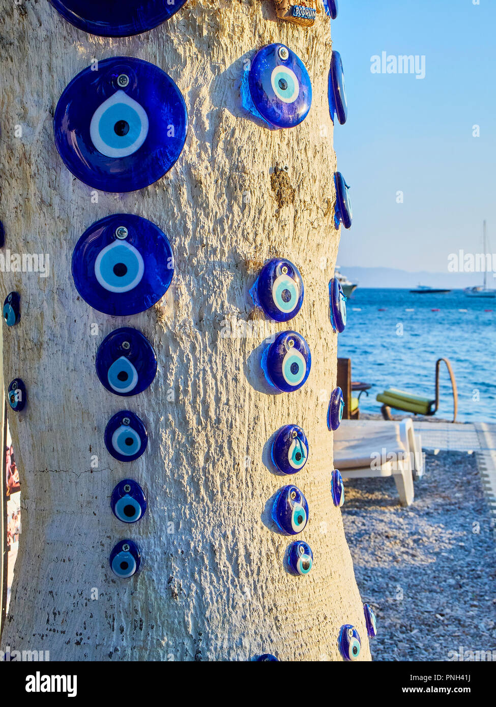 A lot of Nazar boncugu, a Turkish eye-shaped amulet screwed to a tree with the Aegean Sea in the background. Stock Photo
