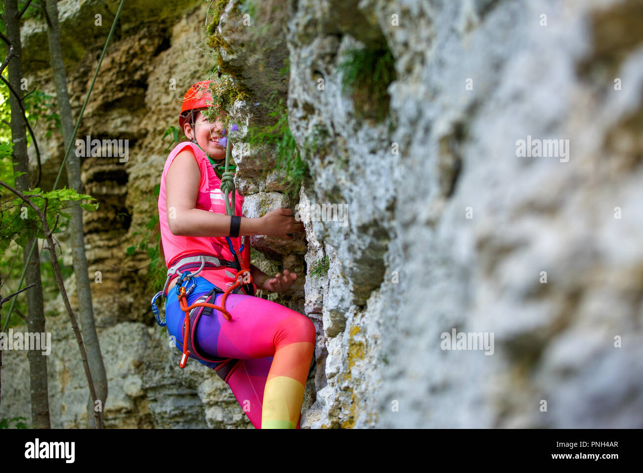 Photo of smiling sports woman in red hard hat climbing up mountain up