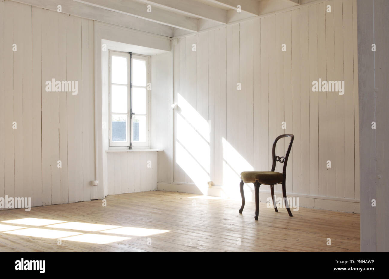 solitary dining chair in white empty room with sunshine through window Stock Photo