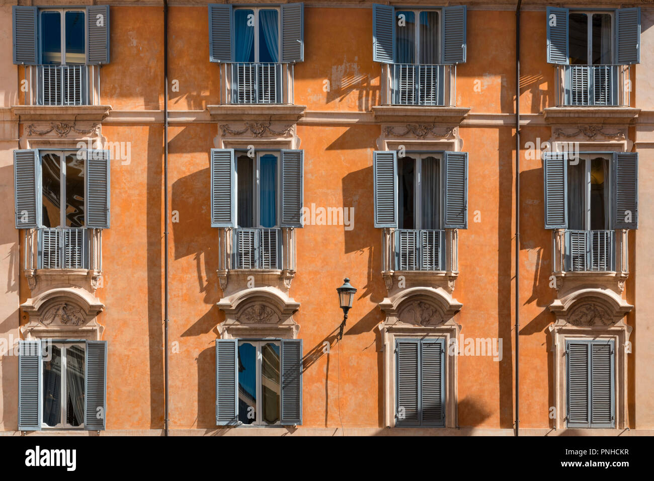 Mediterranean apartments with shutters on a cheerful painted orange sunlit  building facade in the centre of Rome Stock Photo - Alamy, image size:1300x956