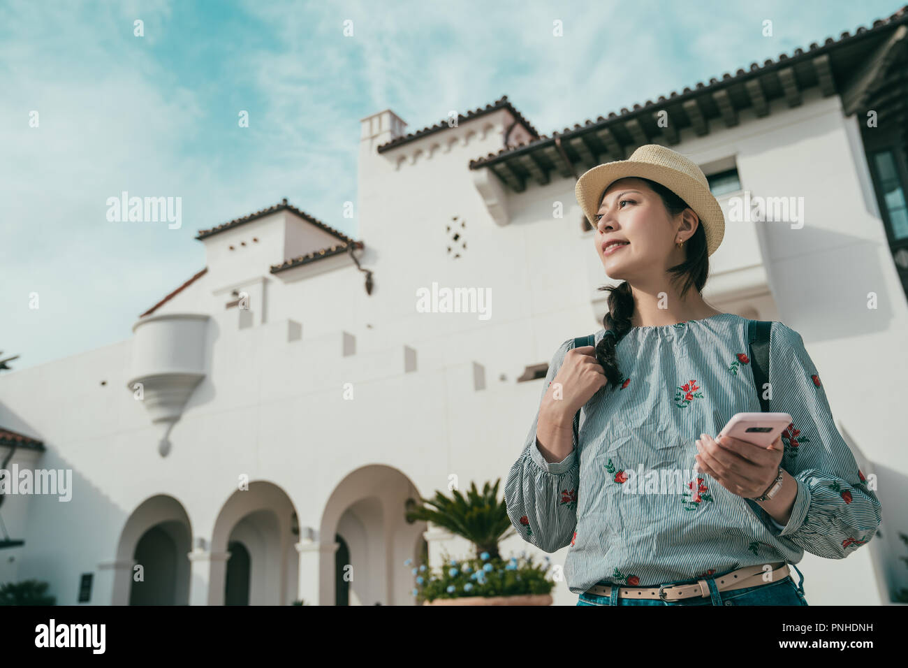 a upward view of a young woman holding a cellphone while visiting a beautiful place in somewhere. Stock Photo