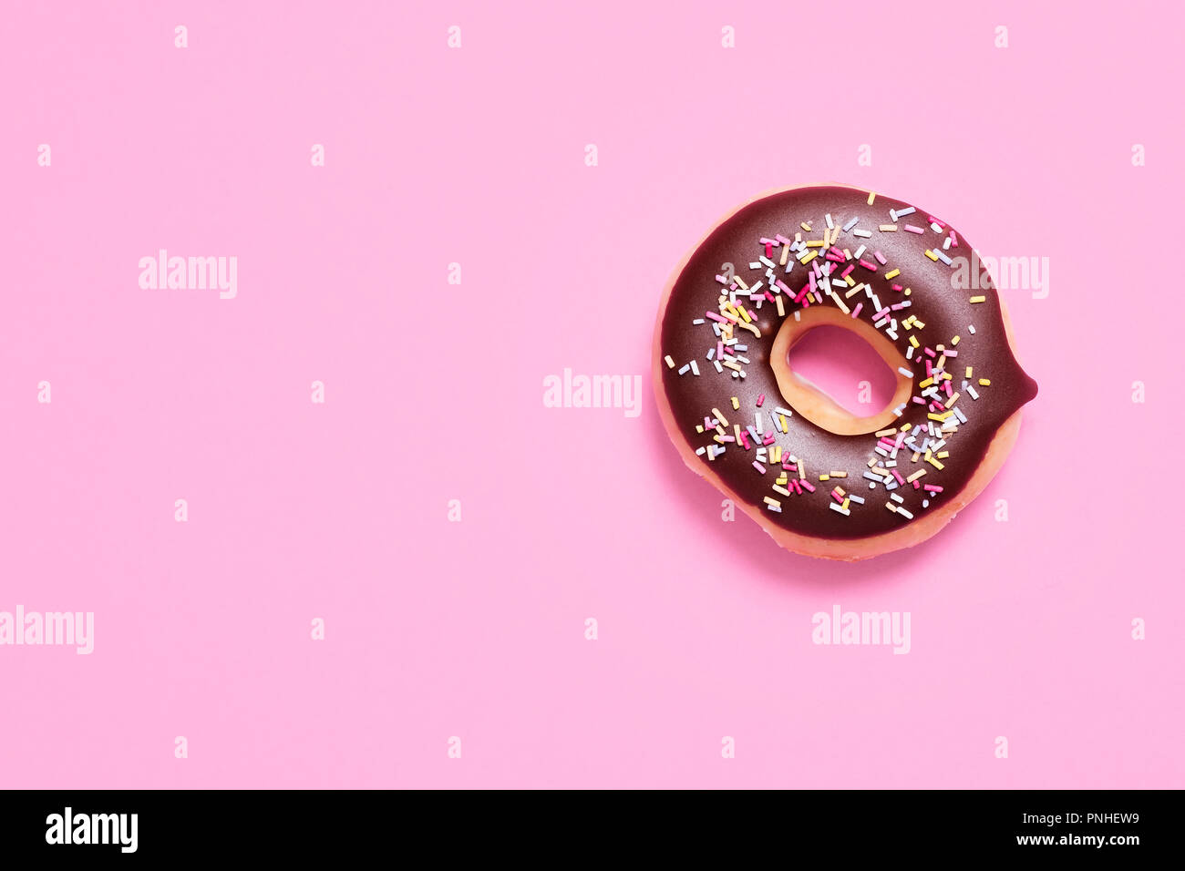Classic ring donut with chocolate frosting and sprinkles on a pastel pink background with space for copy and text Stock Photo