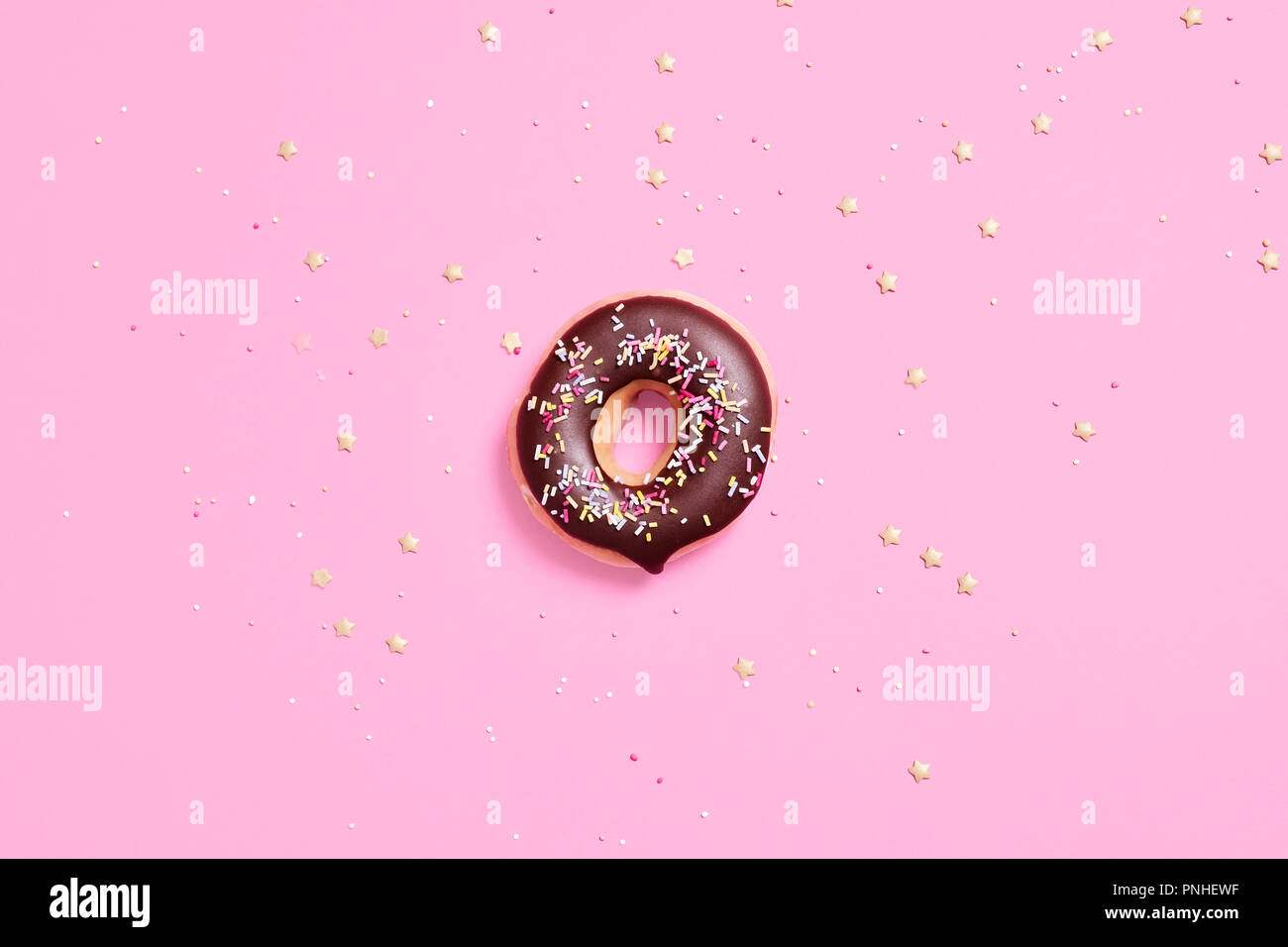Classic ring donuts with chocolate frosting and sprinkles on a pastel pink background with a center composition and sprinkles scattered around. Stock Photo