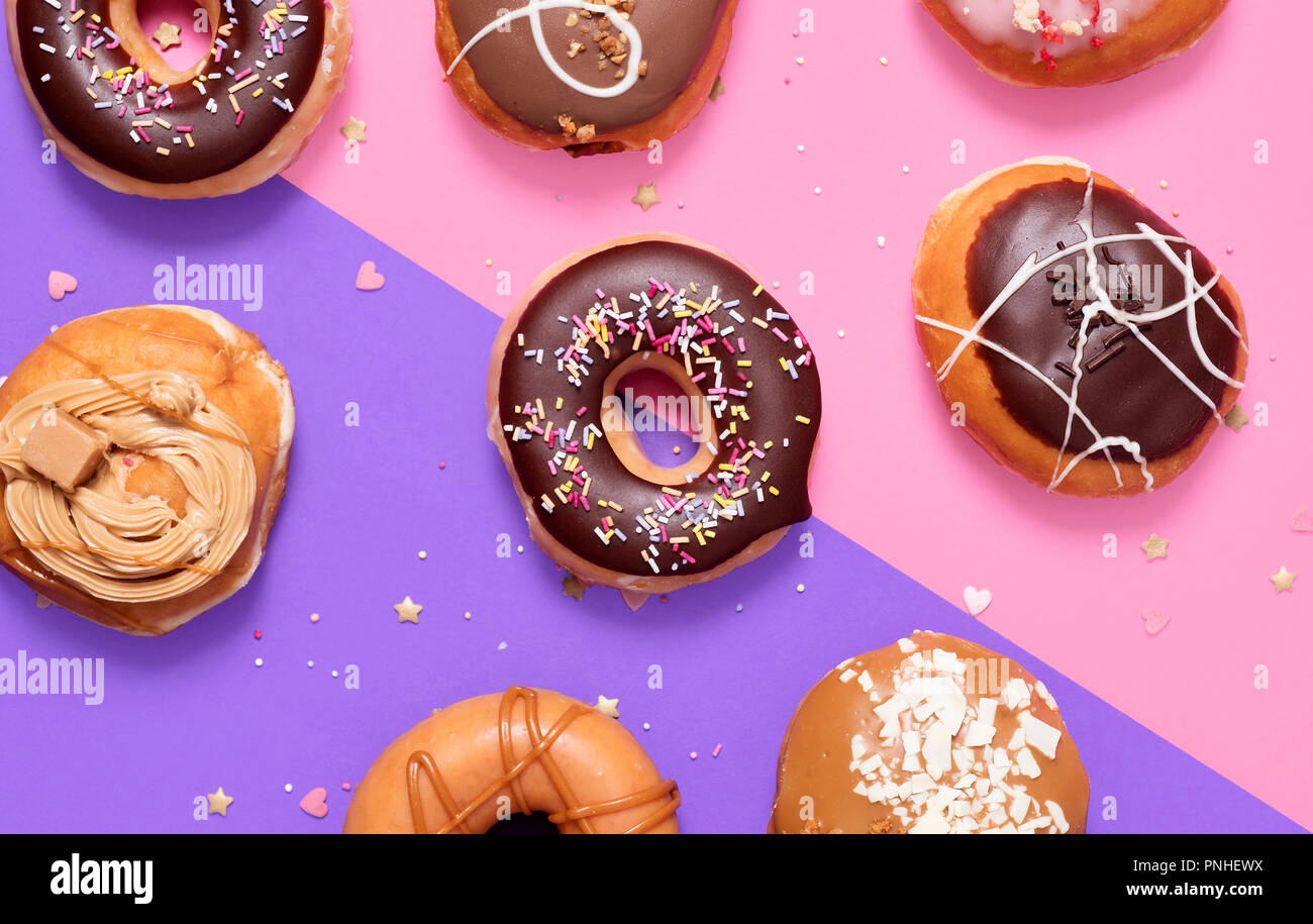 Assorted donuts on a split pink and purple pastel background with a classic chocolate ring and sprinkles donuts in the middle. Stock Photo