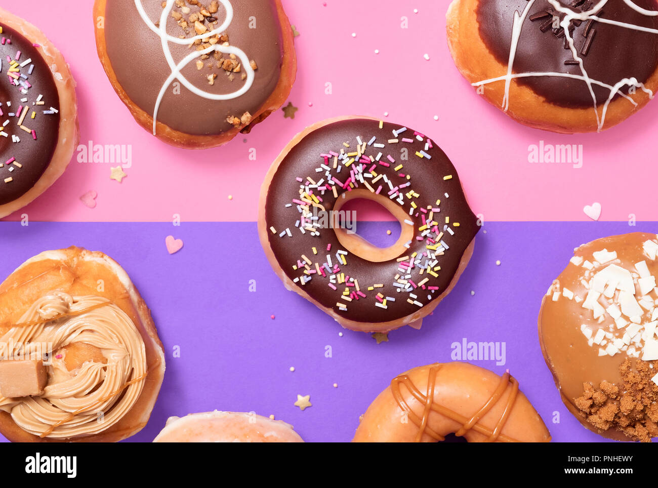 Assorted donuts on a split pink and purple pastel background with a classic chocolate ring and sprinkles donuts in the middle. Stock Photo