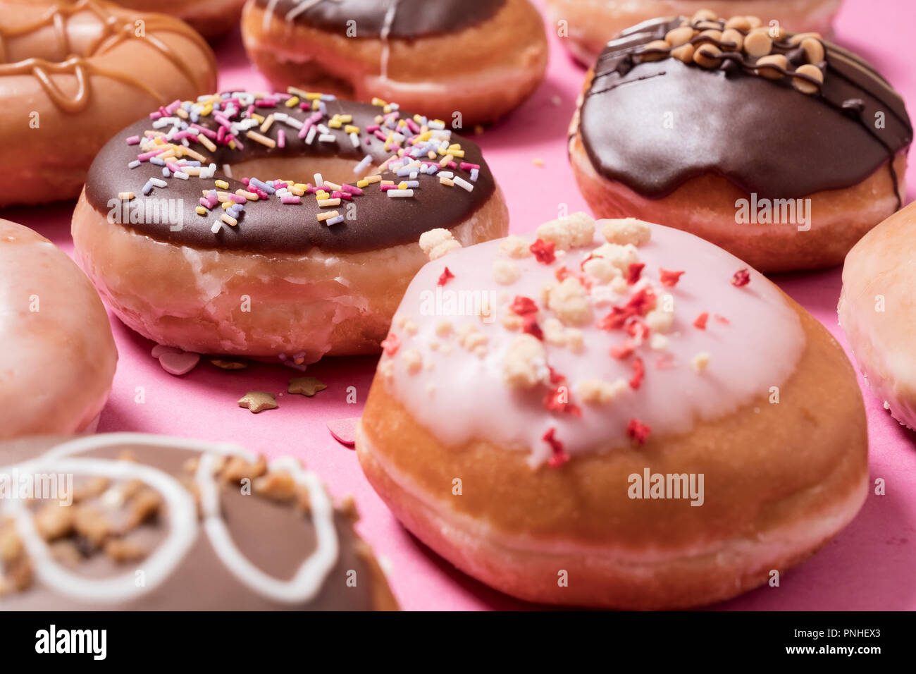 Assorted donuts on a pink background.  Includes classic chocolate sprinkles donut as well as strawberries and cream with scattered sprinkles and heart Stock Photo