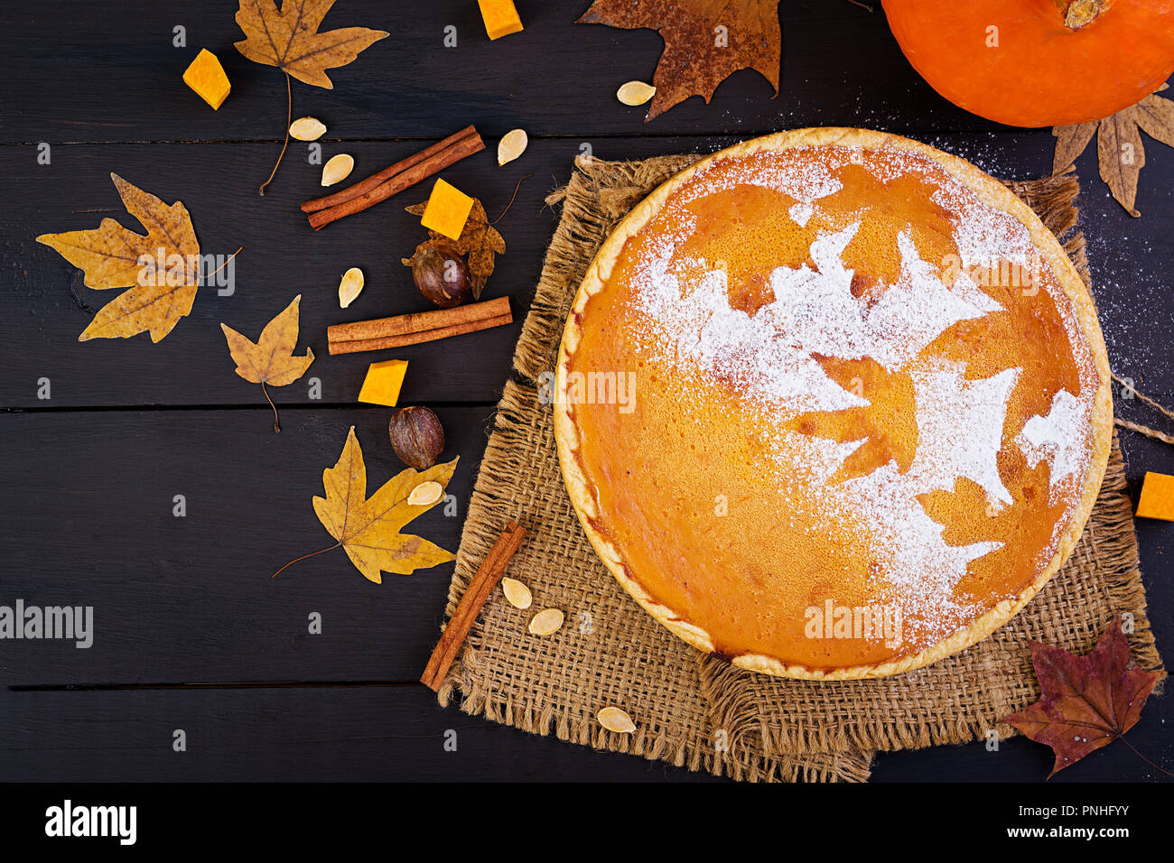 American homemade pumpkin pie with cinnamon and nutmeg, pumpkin seeds and autumn leaves on a wooden table. Thanksgiving food. Top view. Flat lay Stock Photo