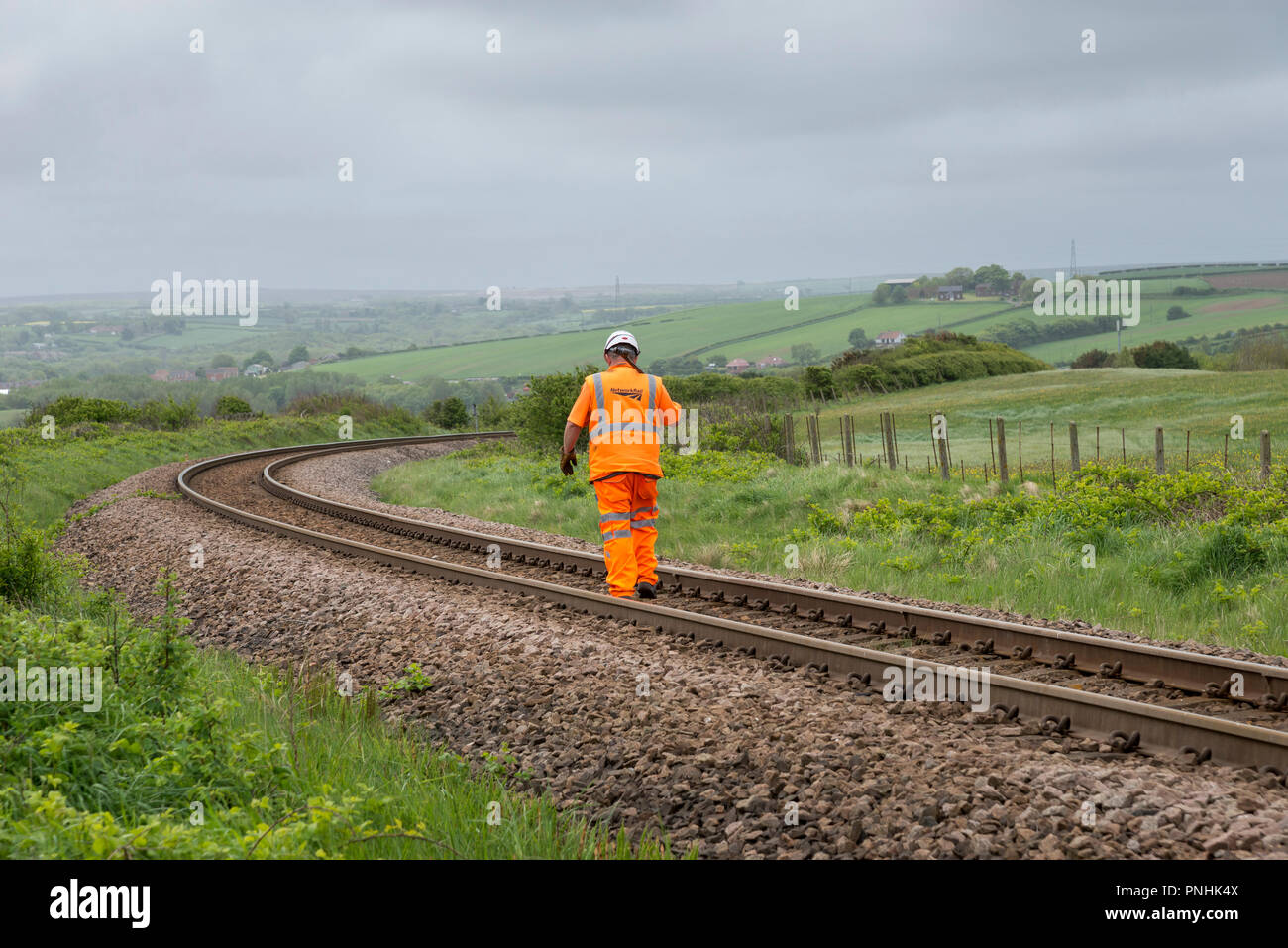 Railway worker in orange work clothes walking along the line at Skinningrove, North Yorkshire. Stock Photo