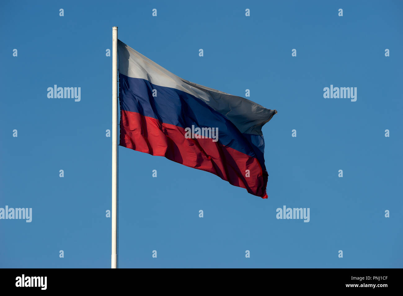 Russian flag of three colors red, blue, white waves in the wind against the background of clean and clear blue sky. Free space to enter text Stock Photo