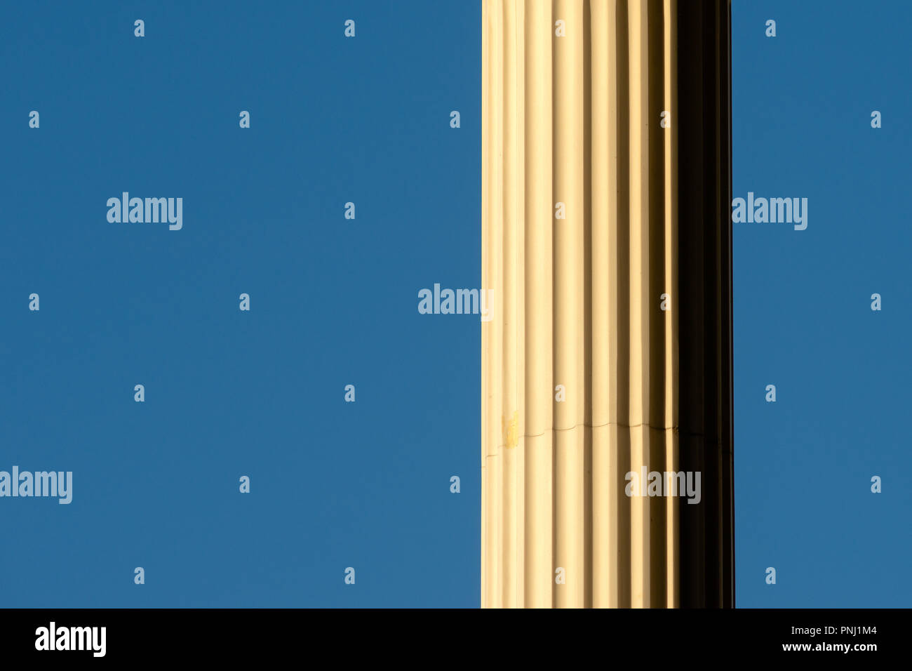 Partly visible sunlit marble column against the background of clear blue sky. Free space to enter text Stock Photo