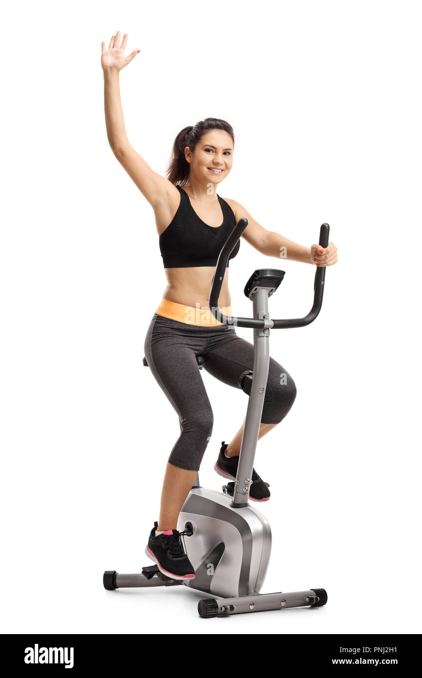 Young woman exercising on a stationary bike and waving isolated on white background Stock Photo