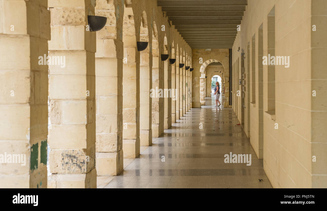 Female tourist walking along a passage with stone archways in Sliema, Malta. Stock Photo