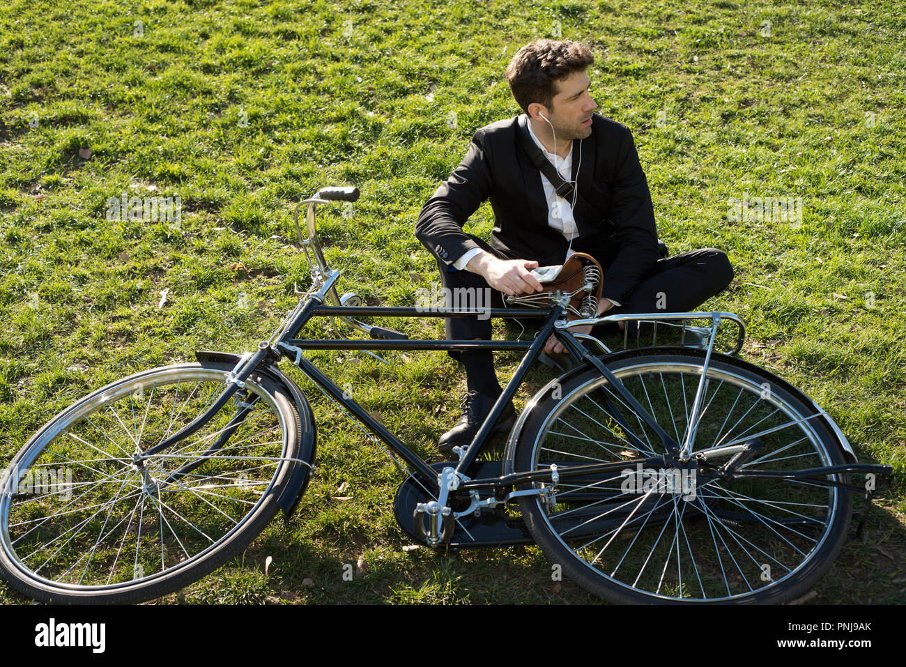 businessman with bicycle listens to earpieces seated in the park Stock Photo