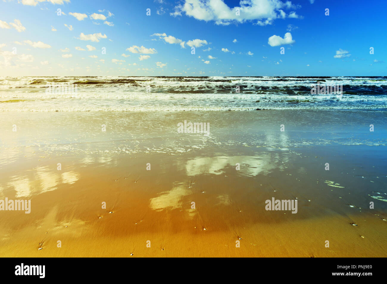 Beautiful seascape with sea waves, blue sky, white cumulus clouds and sandy beach. Summer vacation landscape. Baltic sea, Pomerania, northern Poland. Stock Photo