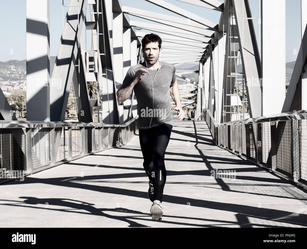 young man running with earpieces by metal bridge Stock Photo