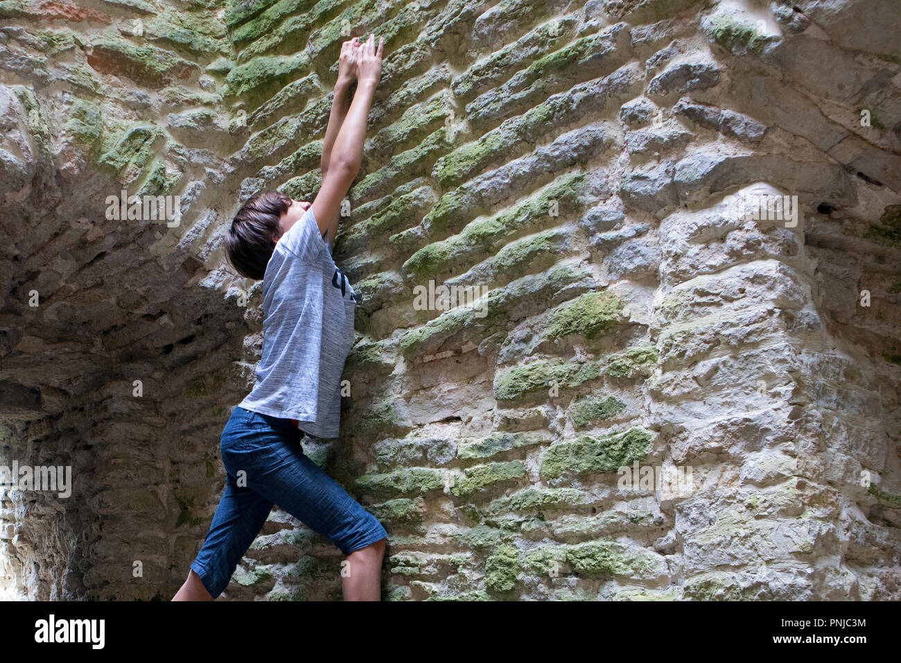 Young boy trying to climb old stone wall inside ancient tower Stock Photo