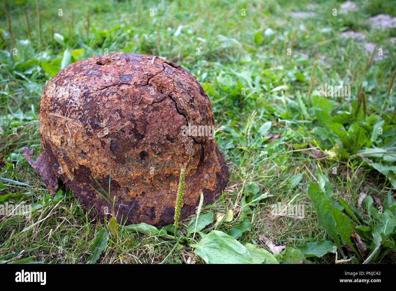 Old rusty german helmet of the Second World War with holes and cracks lying on the grass Stock Photo