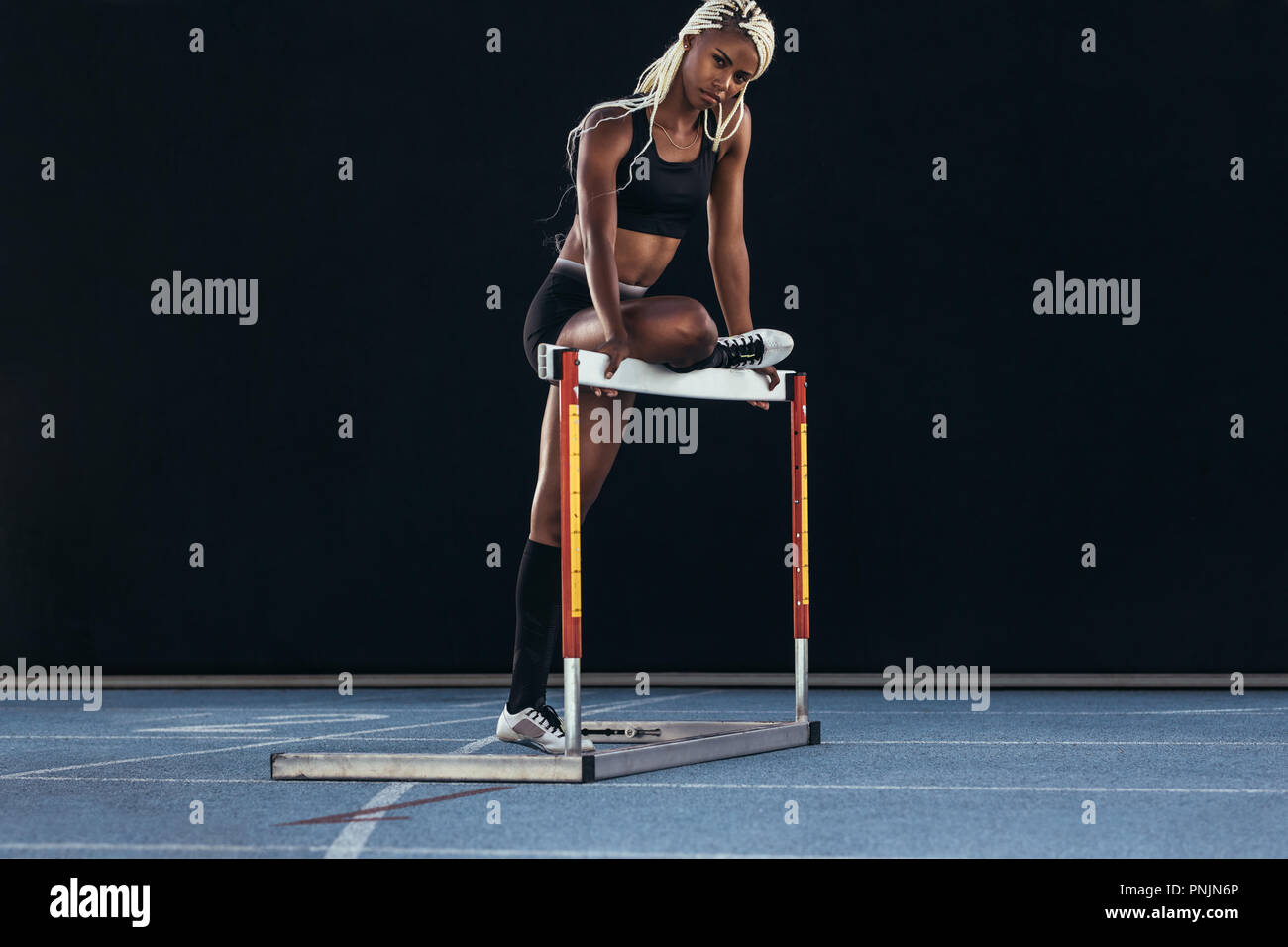 Female athlete standing on a running track resting one leg on a hurdle. Stock Photo
