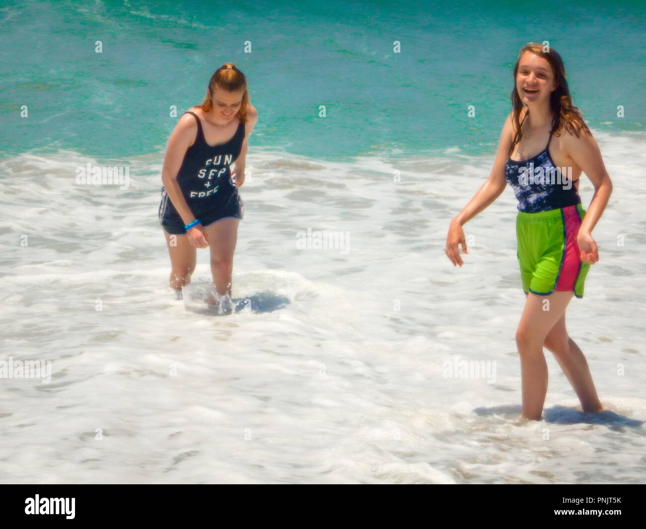 Two girls at the beach have a good time in the ocean waves. Stock Photo