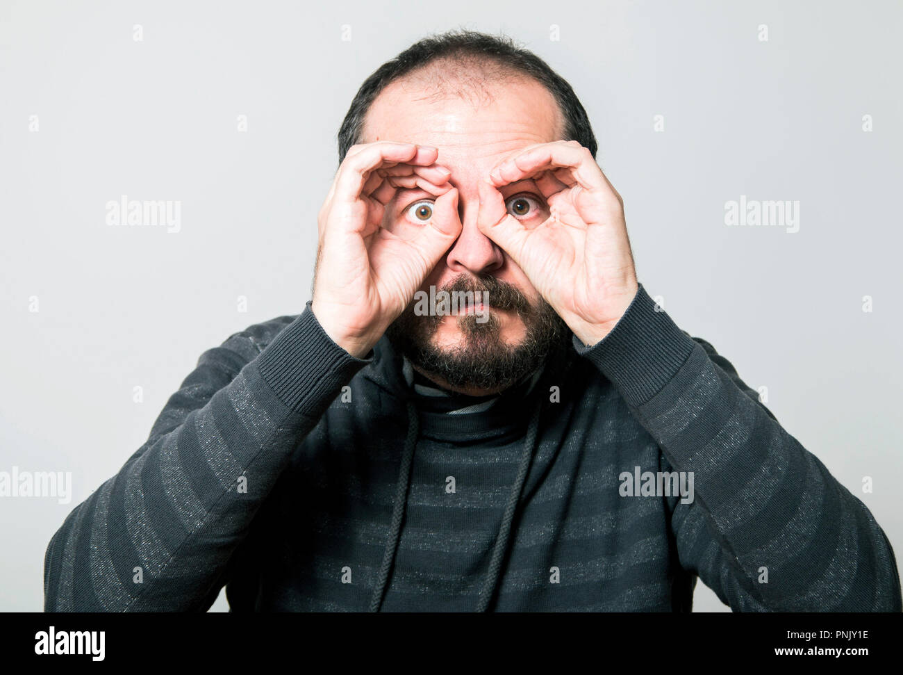 Shocked man looking through hands, making binoculars Stock Photo