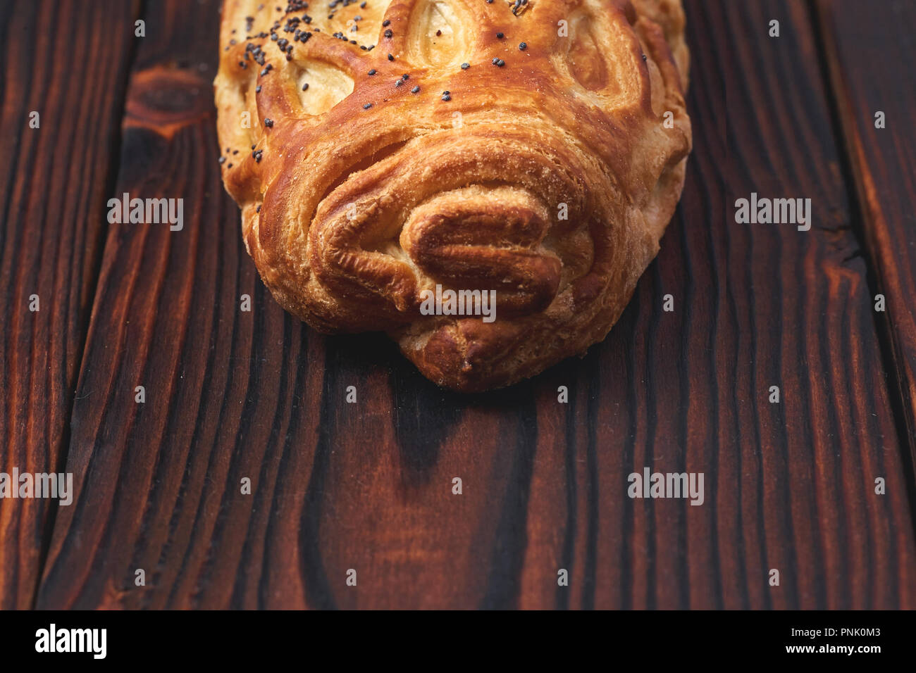 Baked bun with flaky pastry sprinkled with poppy seeds on a dark wooden background. Close-up. Food background. Stock Photo