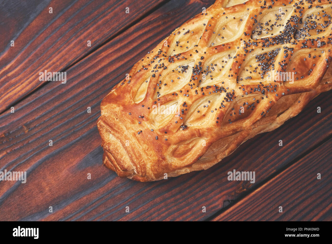 Baked bun with flaky pastry sprinkled with poppy seeds on a dark wooden background. Close-up. Food background. Stock Photo