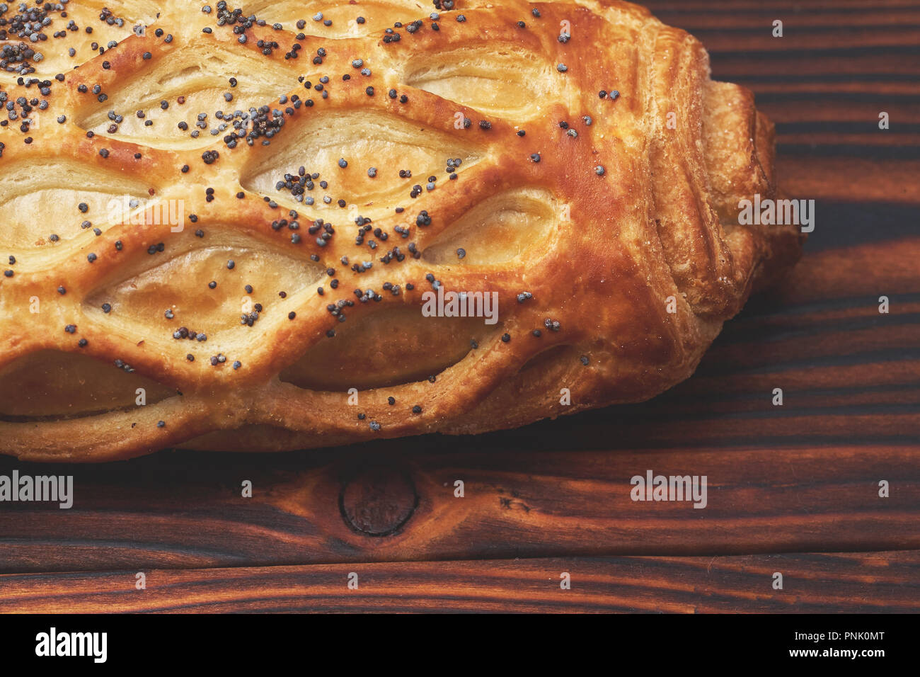 Baked bun with flaky pastry sprinkled with poppy seeds on a dark wooden background. Close-up. Food background. Stock Photo