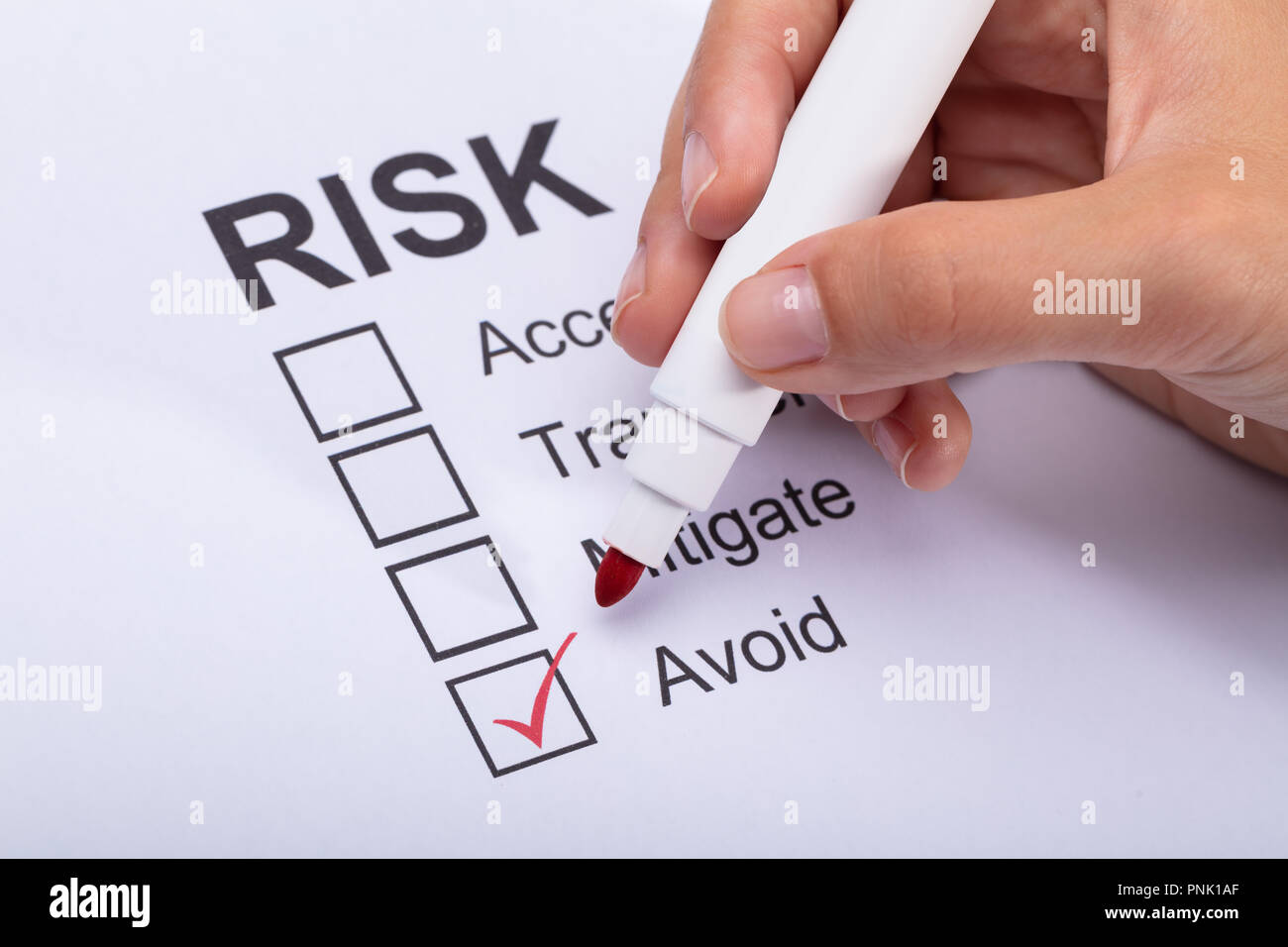 Close-up Of A Woman's Hand Ticking Avoid Option On Risk Form With Marker Stock Photo