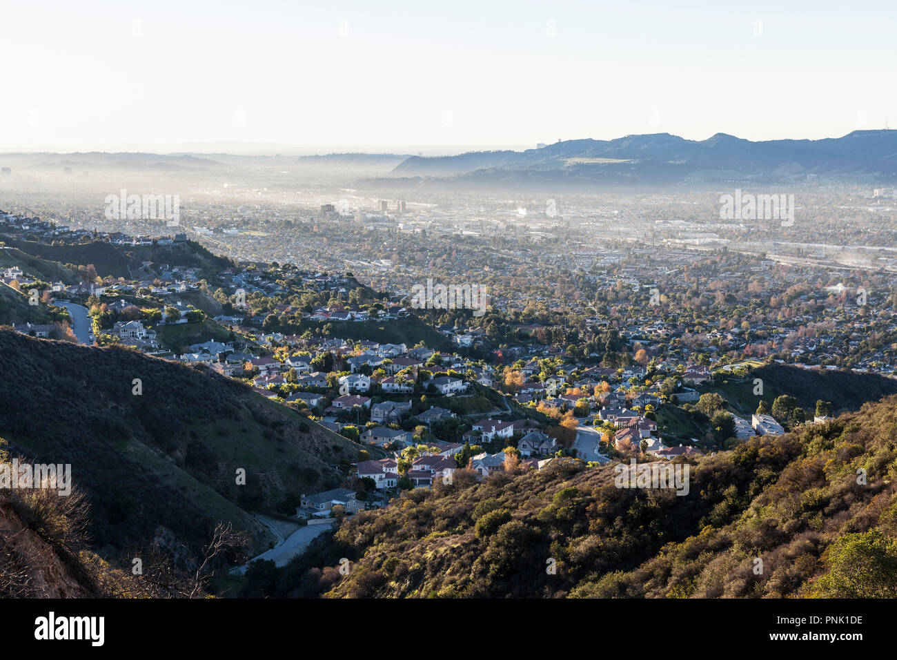 Smoggy hilltop view of canyon homes and downtown Burbank with the San Fernando Valley, the Santa Monica Mountains and Los Angeles California in backgr Stock Photo