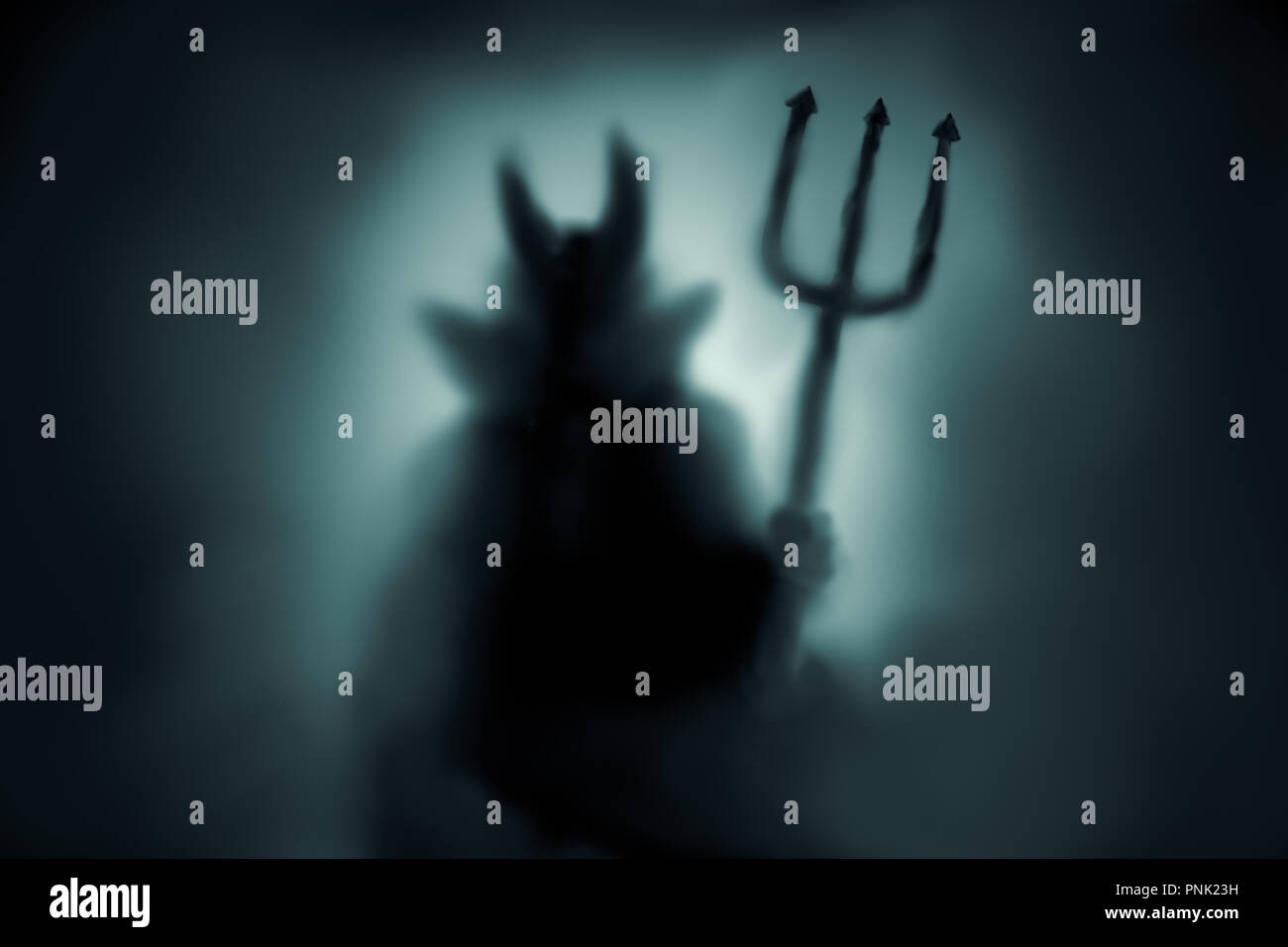 Creepy Devil silhouette behind a frozen glass and in the mist with backlit. Stock Photo