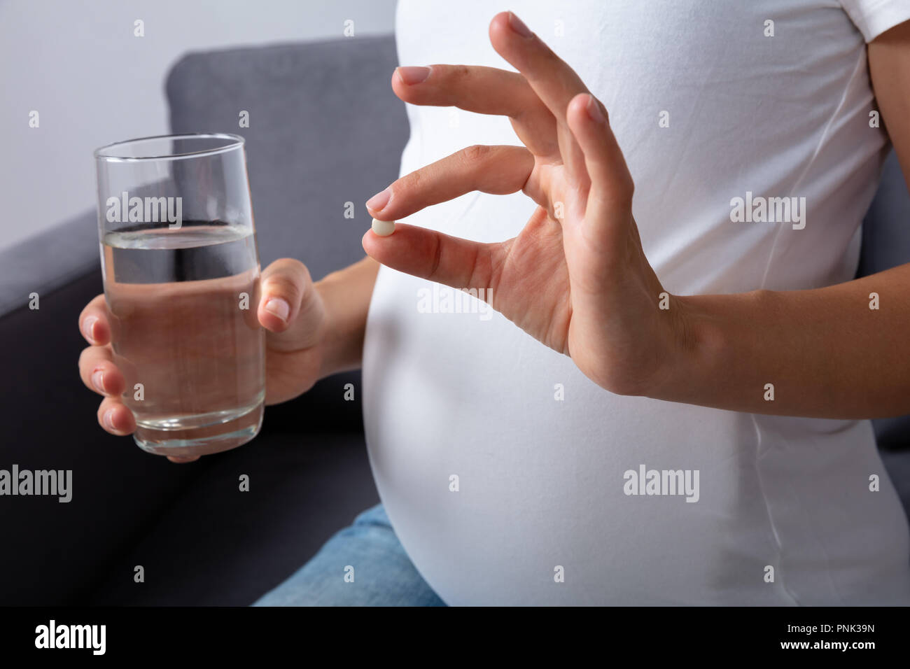 Midsection View Of A Pregnant Woman With Glass Of Water Taking Medicine At Home Stock Photo
