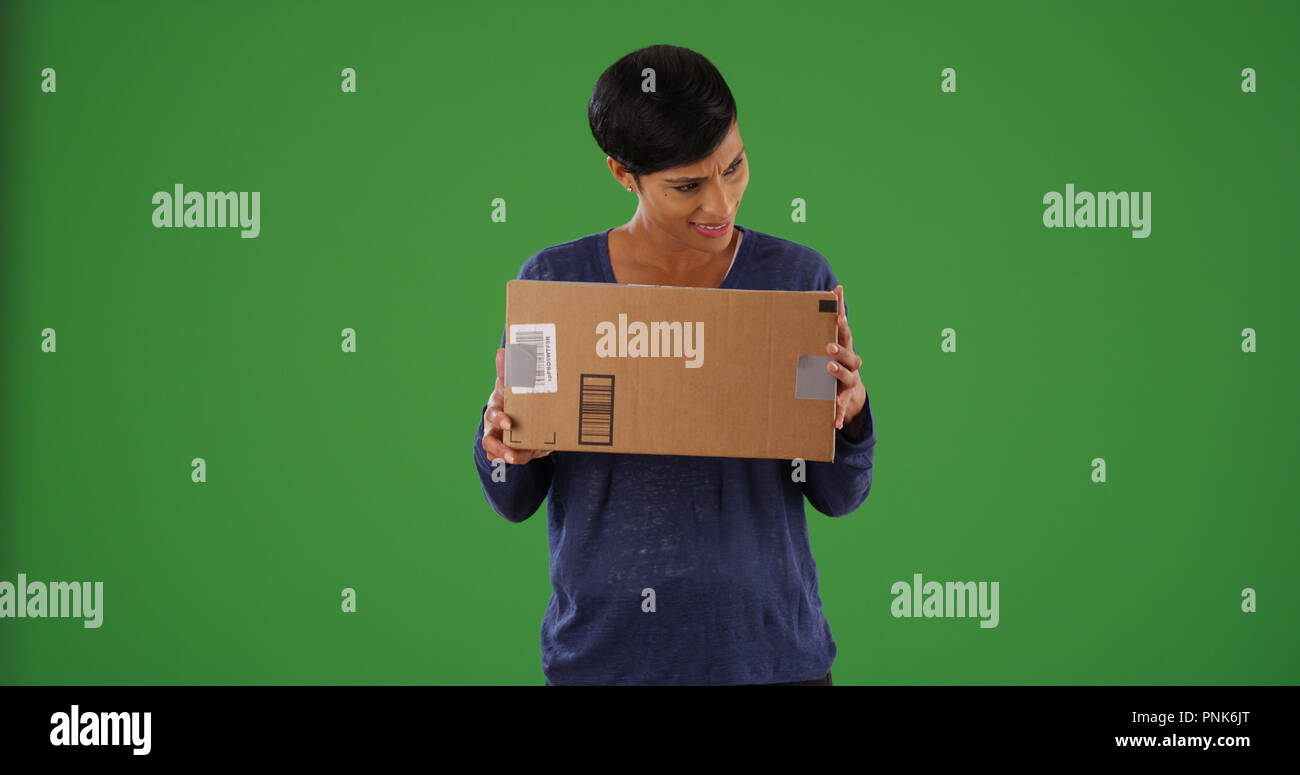 Curious black female shaking cardboard box mail package on green screen ...
