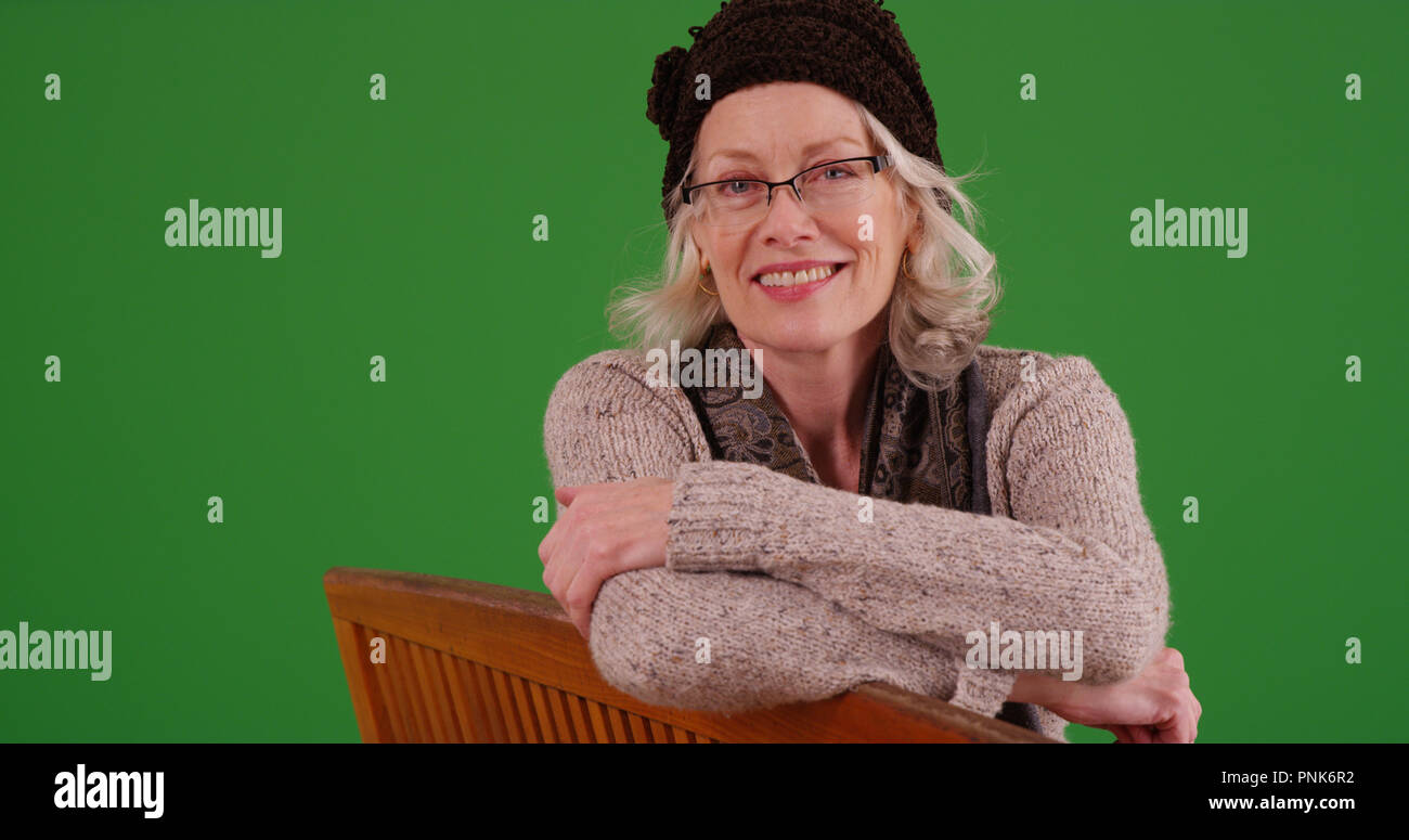 Charming old woman smiling at camera sitting on park bench on green screen Stock Photo