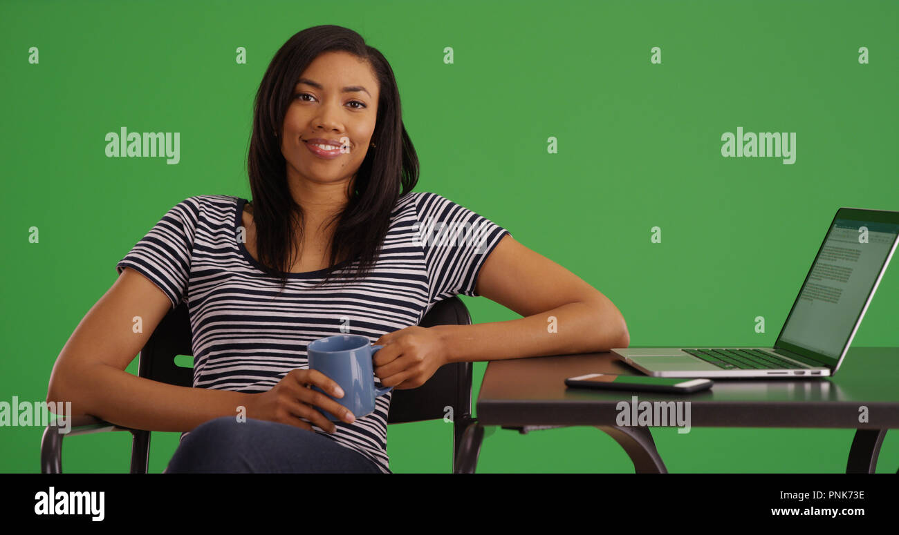 Portrait of smiling black woman with laptop sitting with coffee on ...