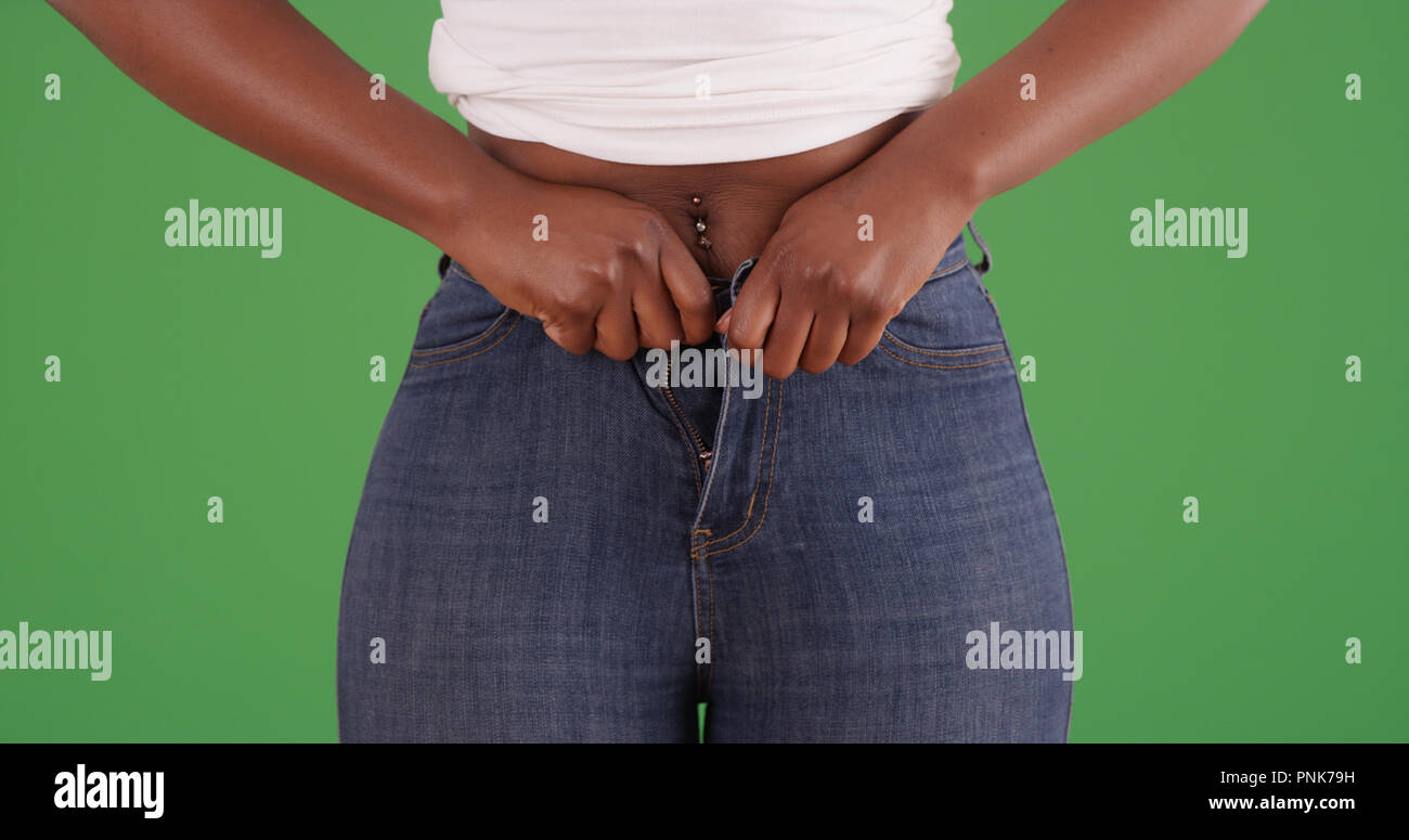 Close up of black female squeezing into small pair of jeans on green screen Stock Photo