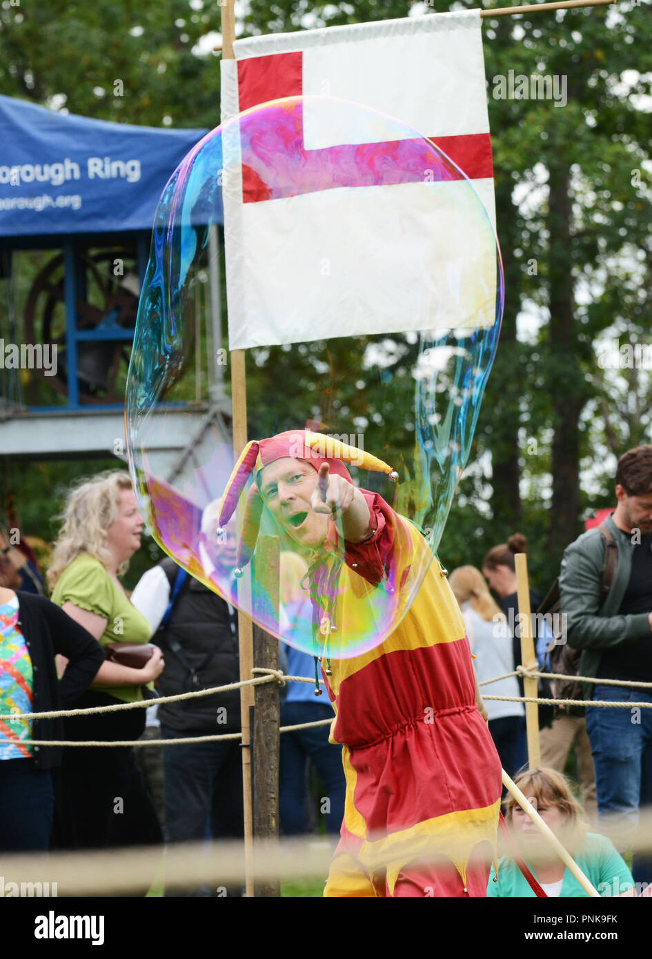 TONBRIDGE, ENGLAND - SEPTEMBER 8, 2018: Bosco the Jester, dressed in medieval costume, points with delight at the floating bubble he has produced for  Stock Photo