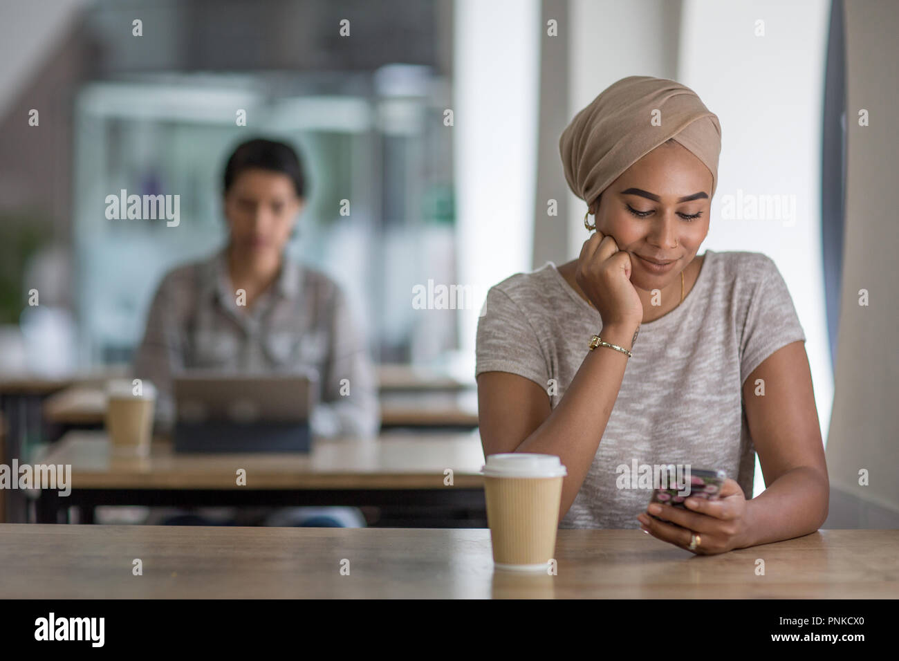 Young adult Muslim female using a smartphone in a cafe Stock Photo