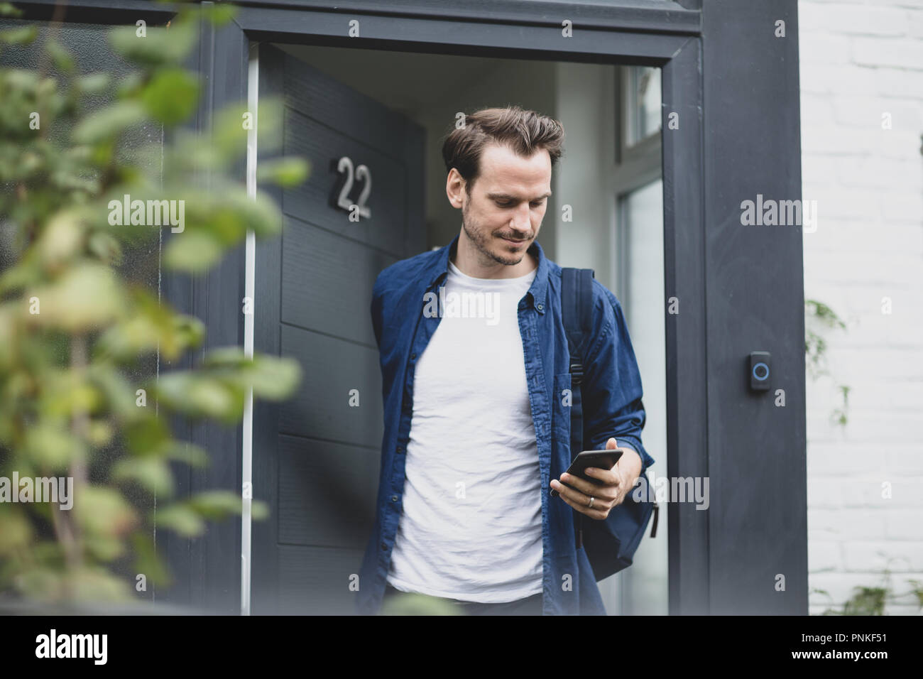 Adult male leaving the house and checking smartphone Stock Photo