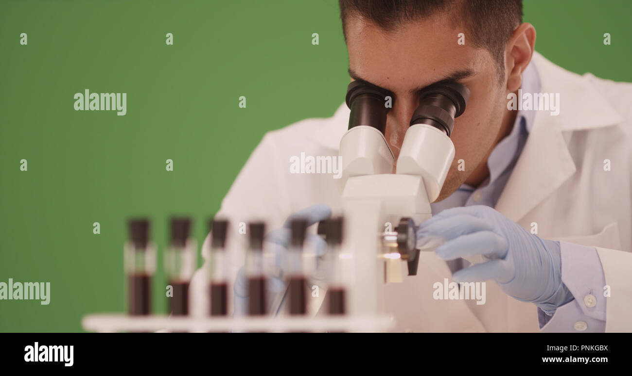 Hispanic medical research scientist in lab using microscope on green