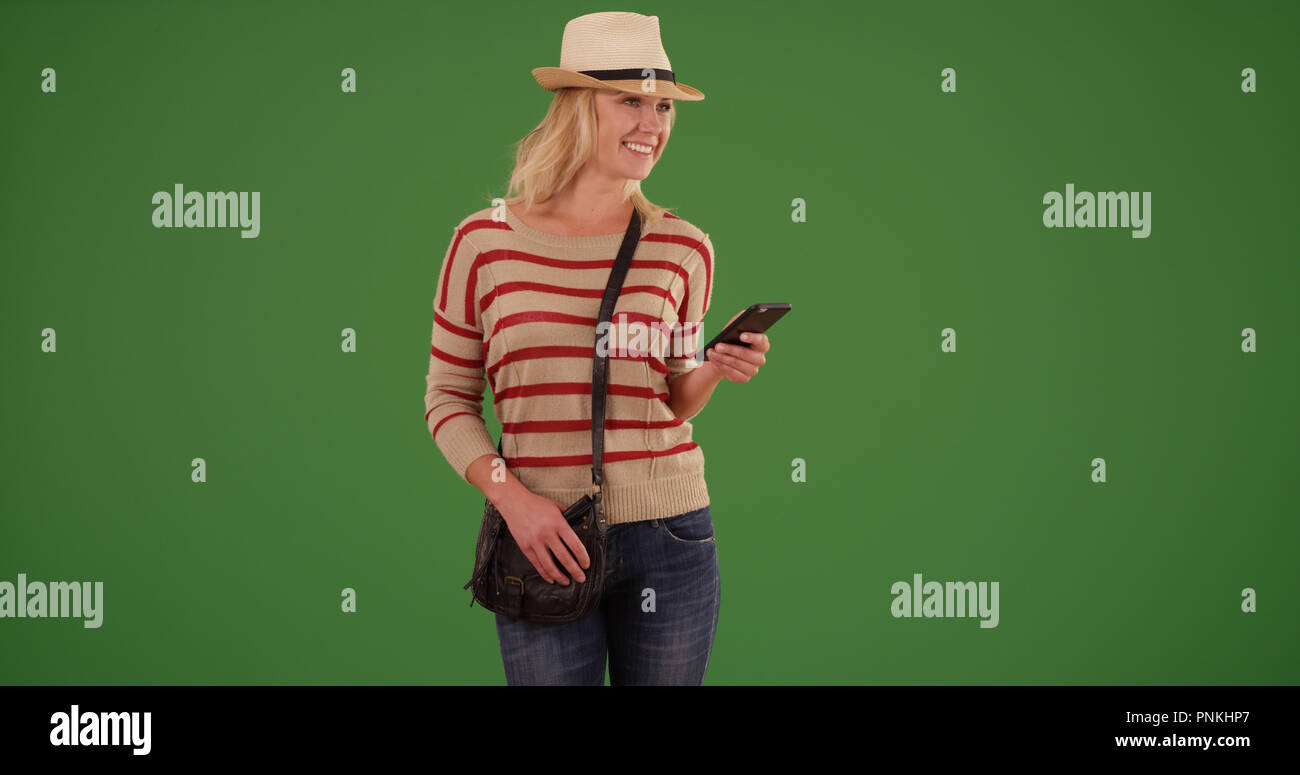 Happy female hipster with smartphone looking happy on green screen Stock Photo