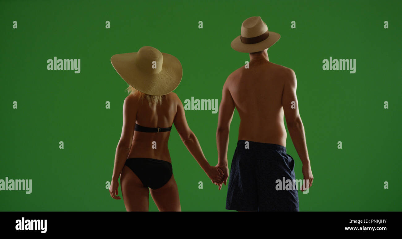 Rear view of couple in hats and swimsuits holding hands on green screen Stock Photo